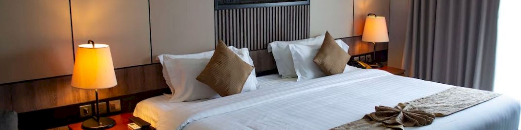 A cozy hotel room with a large bed, two nightstands with lamps, and a wall-mounted decorative feature above the bed.