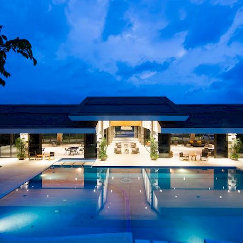 A luxurious outdoor pool and modern building are illuminated at night under a dramatic, cloudy sky.