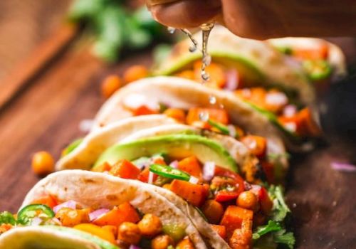 The image shows tacos filled with veggies and chickpeas, garnished with avocado slices and cilantro, with lime being squeezed on top.