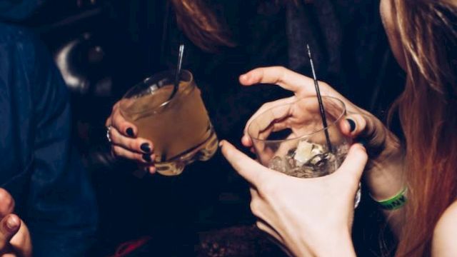 People are gathered, holding drinks with ice, chatting and laughing, possibly at a social event or party, creating a lively atmosphere.
