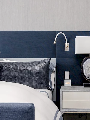 A modern bedroom with a blue and white theme, featuring a bed, a nightstand, a lamp, and a wall light with a sleek design.