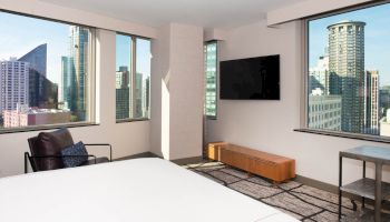 A modern hotel room with a large bed, city skyline views, flat-screen TV, and stylish furniture.