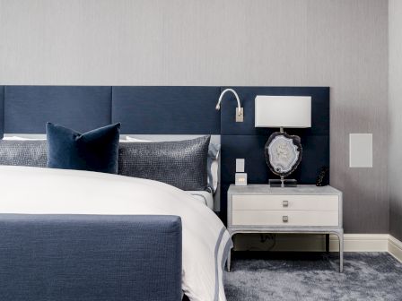 A modern bedroom with a blue headboard, white bedding, and a nightstand featuring a lamp and decorative item.