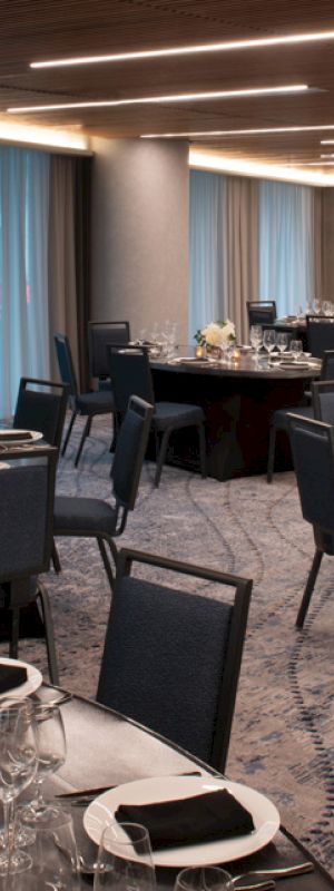 The image shows an elegant banquet hall with round tables set for dining, featuring black and white place settings and soft lighting.