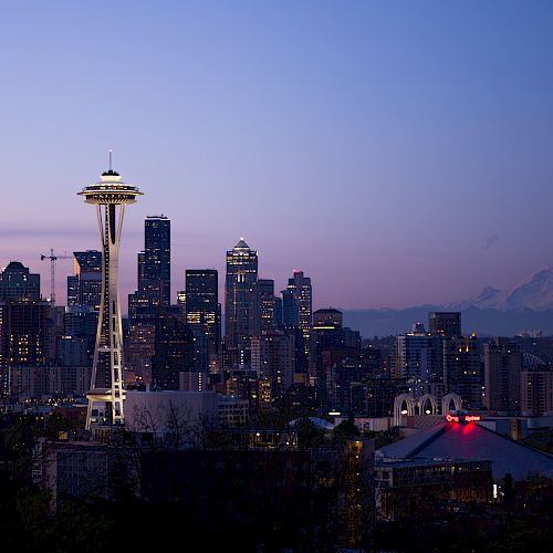 The image shows the Seattle skyline at dusk, featuring the Space Needle and Mount Rainier in the background under a clear sky.