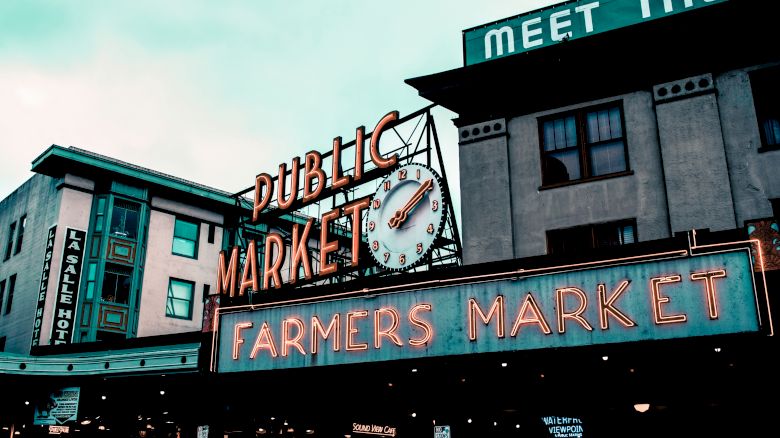 The image shows a public market entrance with neon signs saying "Public Market" and "Farmers Market," featuring a clock.